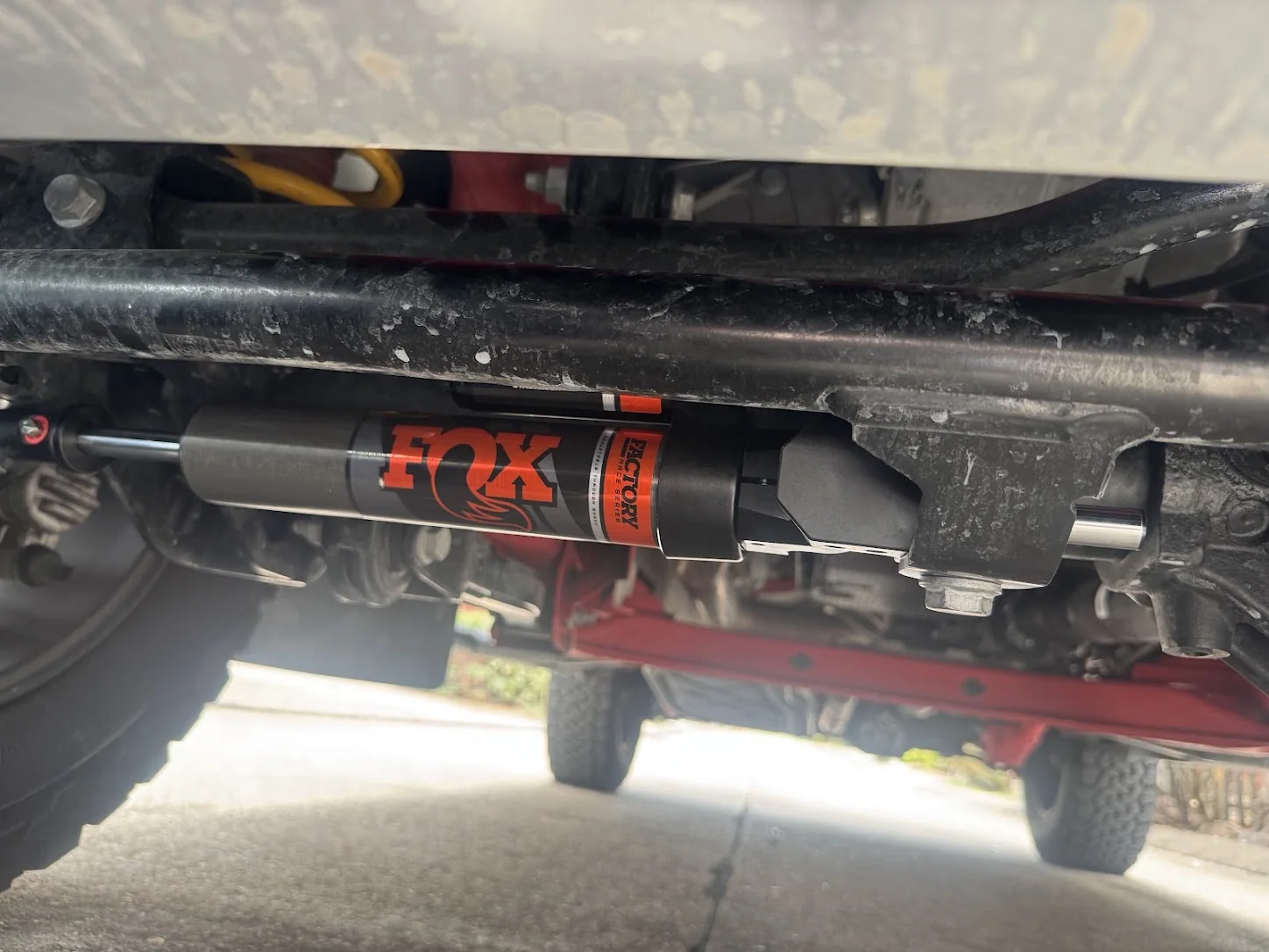 FOX ATS steering stabilizer mounted beneath the Grenadier's front axle, with its red adjuster visible at the left.