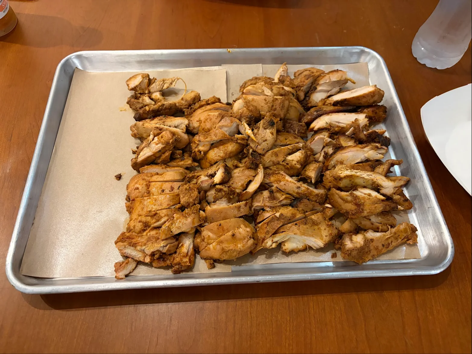 A sheet pan lined with butcher paper and covered in sliced smoked chicken on a wooden table.